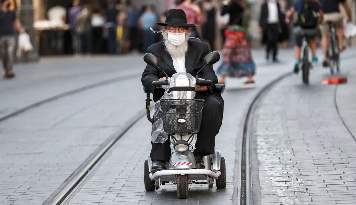 Seorang pria Yahudi Ultra-Ortodoks tua, yang mengenakan masker karena pandemi virus corona COVID-19, mengendarai skuter mobilitas roda tiga di sepanjang jalan di Yerusalem (26/10/2020). (AFP/Emmanuel Dunand)