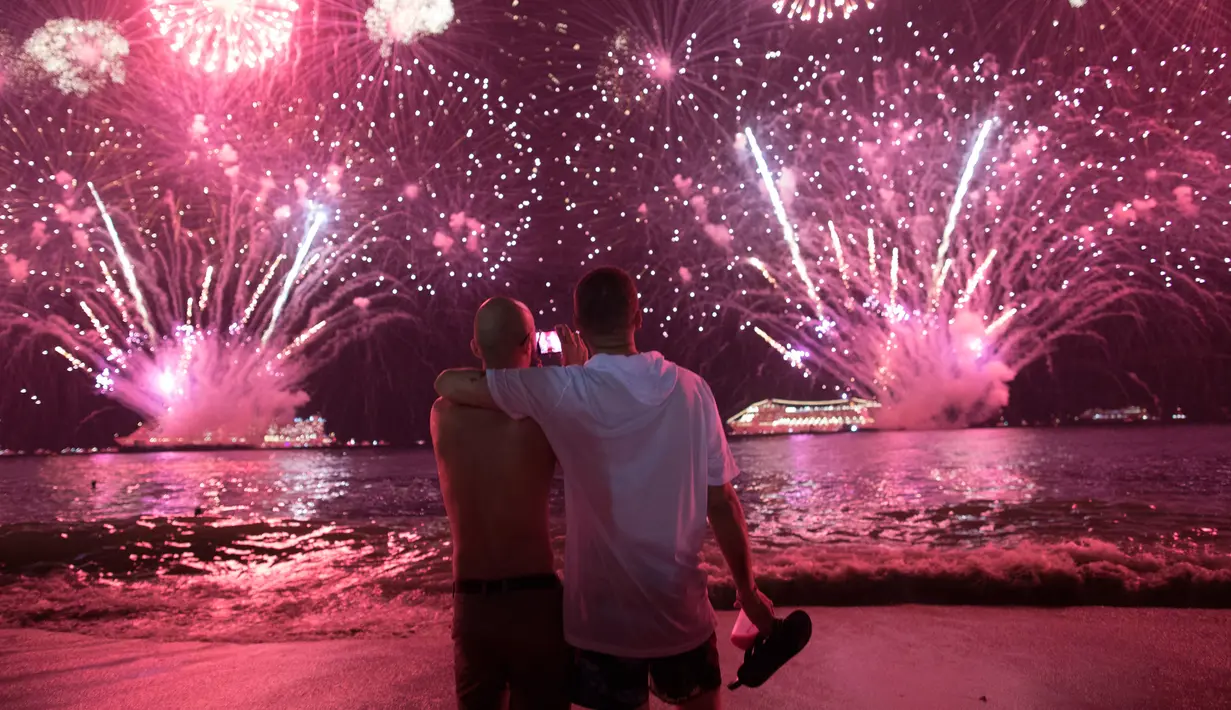 Dua pria berangkulan saat menyaksikan pesta kembang api menyambut Tahun Baru 2019 di Pantai Copacabana, Rio de Janeiro, Brasil, Selasa (1/1). (AP Photo/Leo Correa)