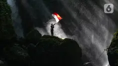 Pengunjung berdiri di atas batu besar sambil memegang bendera Merah Putih di Curug Walet, Pamijahan, Bogor, Jawa Barat, Minggu (24/12/2023). Curug yang terkenal dengan keindahannya ini berada di Desa Ciasihan, Kecamatan Pamijahan. (merdeka.com/Arie Basuki)