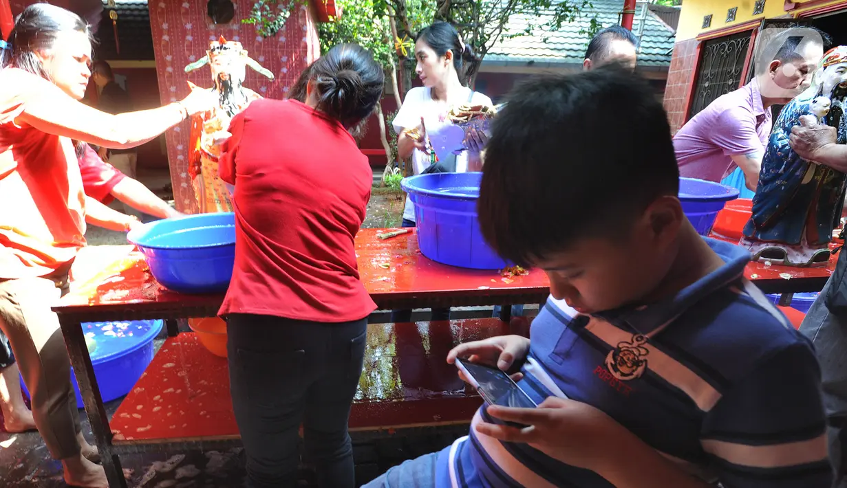 Seorang anak bermain smartphone saat warga keturunan Tionghoa mencuci rupang atau patung dewa dan dewi di Vihara Kwan In Thang, Pondok Cabe, Tangerang Selatan, Banten, Minggu (19/1/2020). Tradisi ini rutin dilakukan jelang Imlek. (merdeka.com/Arie Basuki)
