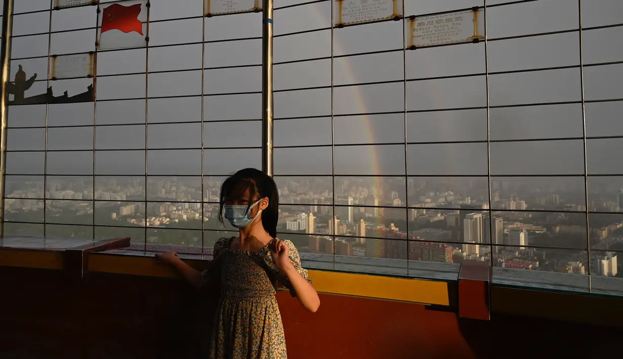 Seorang gadis berpose untuk foto saat pelangi terlihat melalui pagar di Menara Televisi Pusat di Beijing (26/8/2021). Keindahan pelangi ganda dimanfaatkan warga Beijing untuk diabadikan lewat foto dan berfoto dengan latar pelangi itu. (AFP/Jade Gao)