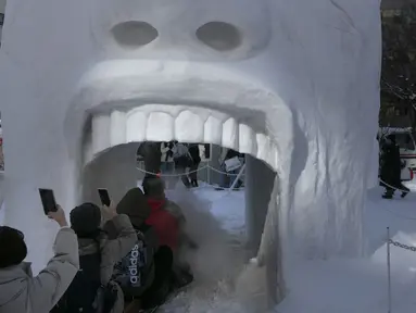 Orang-orang mengambil gambar ketika mereka naik kereta api kecil ke patung salju dalam bentuk mulut manusia selama Festival Salju Sapporo ke-71 di Taman Odori di Sapporo, Jepang, Selasa, (4/2/2020). Festival salju terbesar di Jepang ini Berlangsung hingga bulan Februari. (AP Photo/Jae C. Hong)