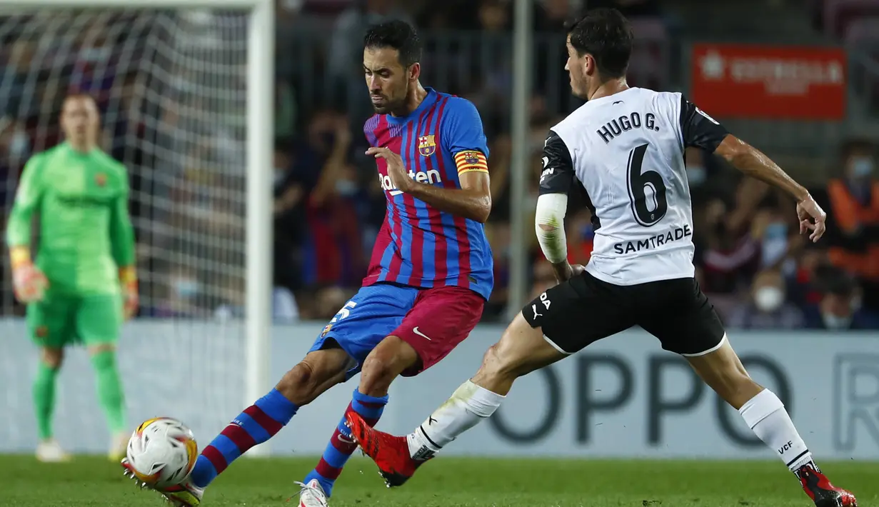 Gelandang Barcelona, Sergio Busquets berusaha mengumpan bola dari kawalan pemain Valencia, Hugo Guillamon pada pertandingan lanjutan La Liga Spanyol di stadion Camp Nou,Spanyol, Senin (18/10/2021). Barcelona menang atas Valencia dengan skor 3-1. (AP Photo/Joan Monfort)