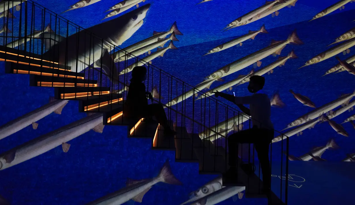 Seorang pria mengambil foto wanita berpose di galeri seni digital Infinity des Lumieres di Dubai Mall, Dubai, Uni Emirat Arab, Senin (12/7/2021). Infinity des Lumieres menggunakan proyektor digital untuk memutar gambar bergerak karya seni di galeri besar. (AP Photo/Jon Gambrell)