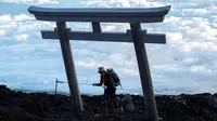 Seorang pria mencapai puncak Gunung Fuji, barat Tokyo pada 18 Juli 2021. Mendaki Gunung Fuji bukanlah hal yang mudah, tetapi pemandangan matahari terbit di atas lautan awan adalah hadiah terindah bagi yang mencapai puncak tertinggi di Jepang. (Charly TRIBALLEAU/AFP)