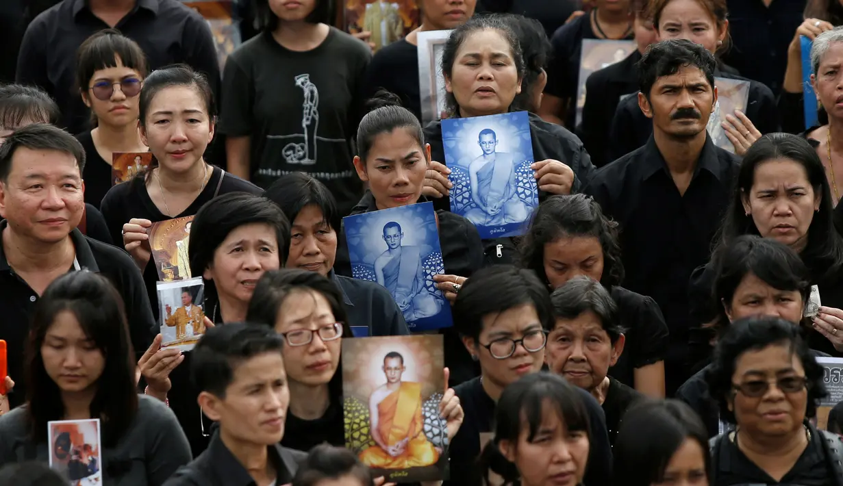 Sejumlah pelayat memegang foto Raja Bhumibol Adulyadej saat berkumpul di luar Grand Palace sambil menyanyikan rekaman lagu kerajaan, di Bangkok, Thailand, (22/10). Malamnya para pelayat akan menyalakan lilin dan menyanyikan lagu. (REUTERS/Jorge Silva)