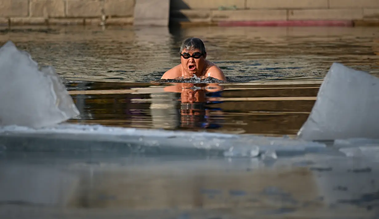 Seorang pria berenang di sungai yang sebagian membeku di Beijing, China (10/1). Akibat membeku, Sungai ini menjadi objek wisata dadakan. (AFP Photo/Wang Zhao)
