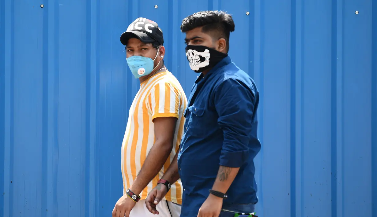 Dua pria mengenakan masker berjalan di sepanjang jalan di New Delhi (16/9/2020). Total kasus Covid-19 di India melampaui lima juta pada 16 September, data kementerian kesehatan menunjukkan Pandemi meluas cengkeramannya di negara tersebut. (AFP/Sajjad Hussan)