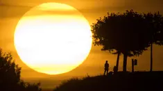 Orang-orang terlihat siluet saat berjalan-jalan selama matahari terbenam di bukit Kronberg di Hannover, Jerman utara (6/8). (AP Photo/Julian Stratenschulte)
