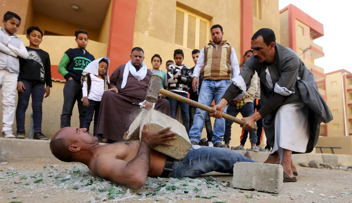 Beralaskan pecahan kaca, Karim Hussein menahan batu yang dipecahkan dengan palu besar dengan perutnya saat unjuk kebolehan di Kairo (18/3/2016). Aksi mengerikannya ini menjadi tontonan warga sekitar. (Reuters/ Mohamed Abd El Ghany)