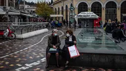 Perempuan yang mengenakan masker berbicara satu sama lain di alun-alun Monastiraki di pusat kota Athena, Yunani, Rabu (29/12/2021). Organisasi Kesehatan Dunia (WHO) memperingatkan lonjakan kasus Covid-19 varian Omicron dapat menyebabkan fasilitas kesehatan kewalahan. (Angelos Tzortzinis/AFP)