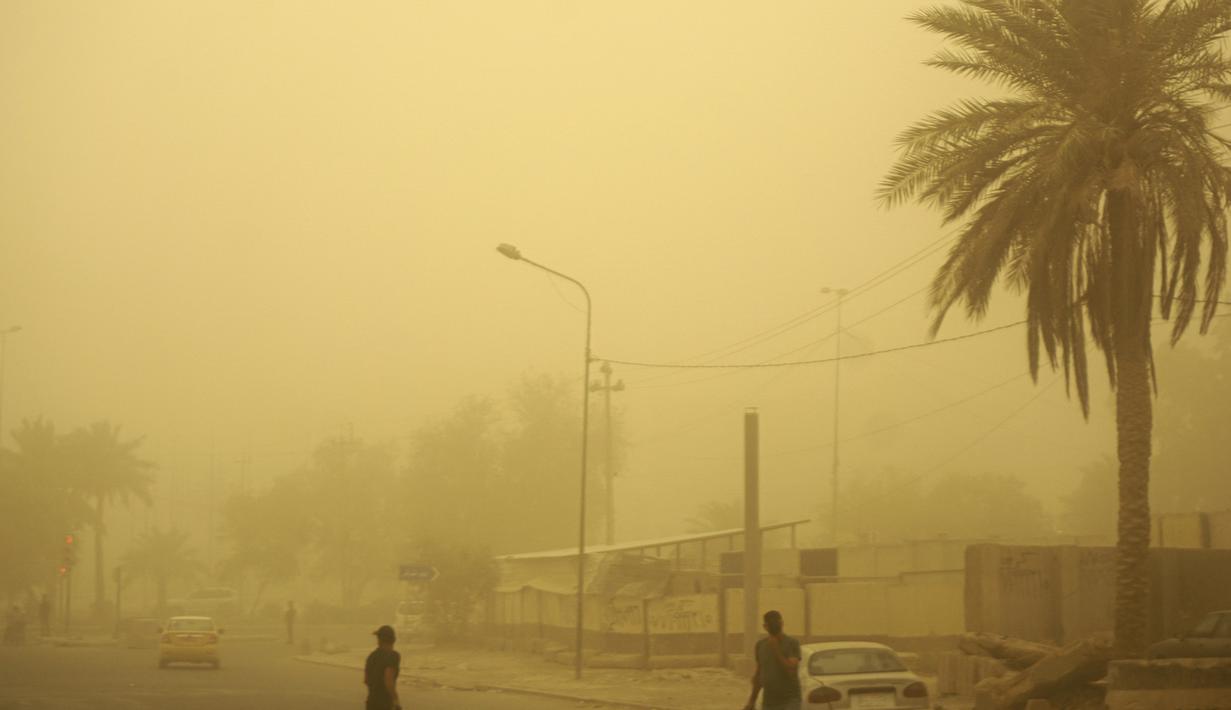 Orang-orang berjalan di jalan di ibu kota Irak, Baghdad, saat debu tebal akibat badai pasir menyelimuti kota itu, pada Senin (23/5/2022). Irak menutup bandara dan gedung-gedung publik saat badai pasir -- yang kesembilan sejak pertengahan April -- melanda negara itu, kata pihak berwenang. (Sabah ARAR / AFP)