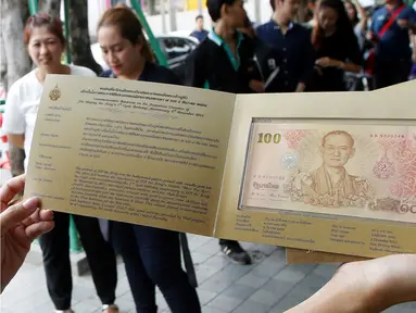Seorang warga menunjukkan uang kertas 100 baht yang bergambar mendiang raja Thailand Bhumibol Adulyadej di Bangkok, Thailand (18/10). Uang 100 baht edisi ini dibuat untuk memperingati ulang tahun raja ke-84. (Reuters/Edgar Su)