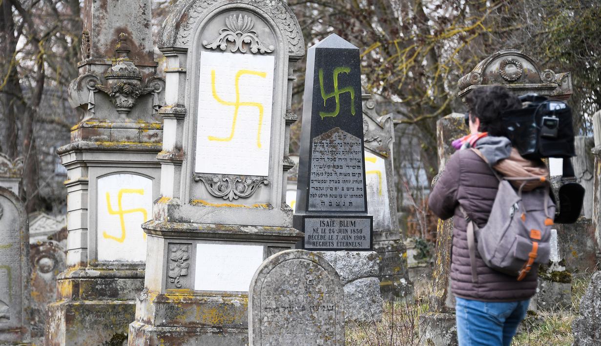 Seorang jurnalis mengambil gambar makam Yahudi yang dicoret simbol Nazi di pemakaman Yahudi, Quatzenheim, Prancis, Selasa (19/2). Prancis merupakan negara Eropa dengan komunitas Yahudi terbanyak yaitu sekitar 550 ribu orang. (Frederick FLORIN/AFP)