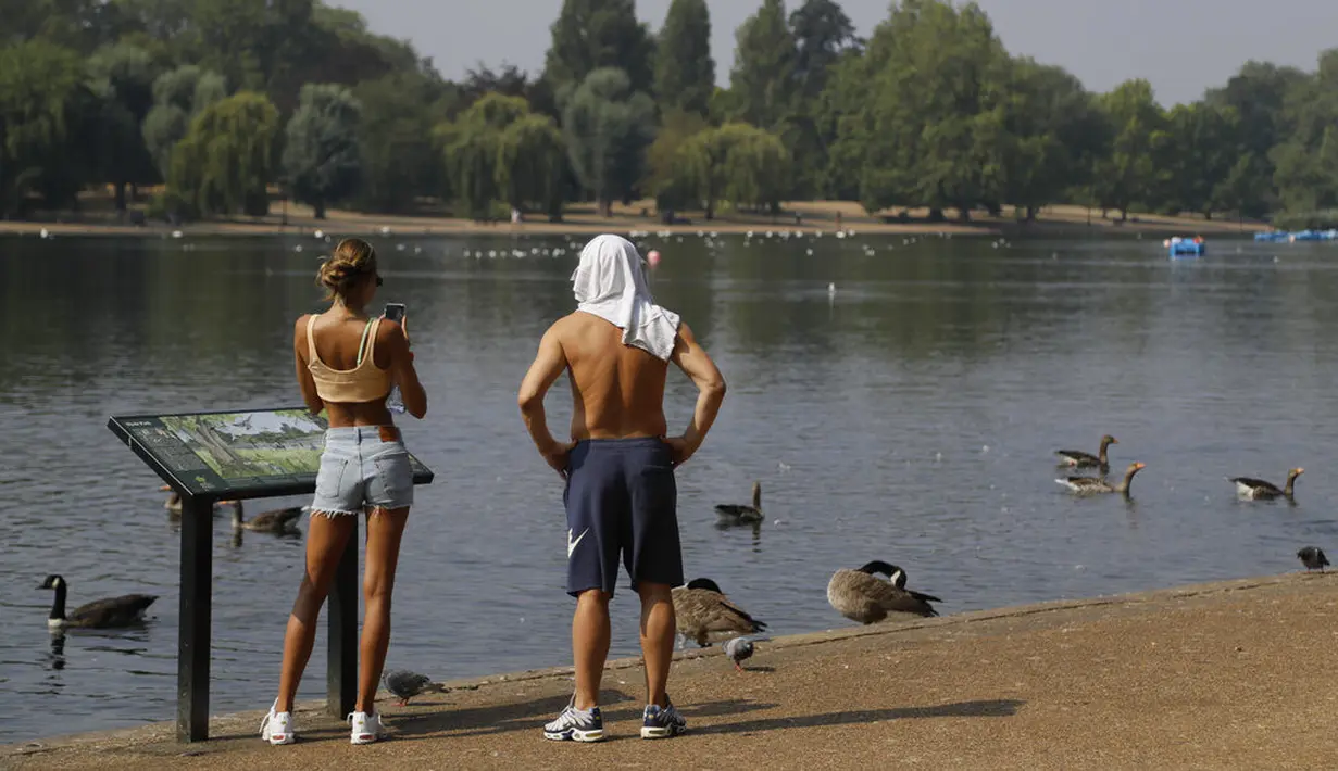 Seorang pria dan wanita menikmati suasana sungai Serpentine di Hyde Park di London, Rabu, (12/8/2020). Peringatan badai masih berlaku untuk sebagian besar Inggris pada hari Rabu, sementara suhu tinggi diperkirakan lagi di banyak bagian Inggris. ( AP Photo / Kirsty Wigglesworth)