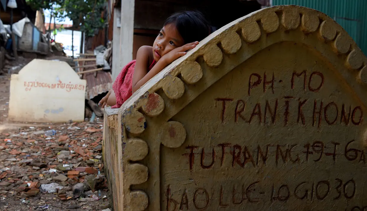 Seorang anak perempuan berbaring di atas sebuah kuburan di Phnom Penh, Kamboja pada 5 Juni 2019. Pemakaman menjadi tempat peristirahatan abadi bagi orang mati, tetapi area pemakaman ini menjelma sebagai tempat tinggal untuk bertahan hidup bagi mereka yang didera kemiskinan. (TANG CHHIN Sothy/AFP)