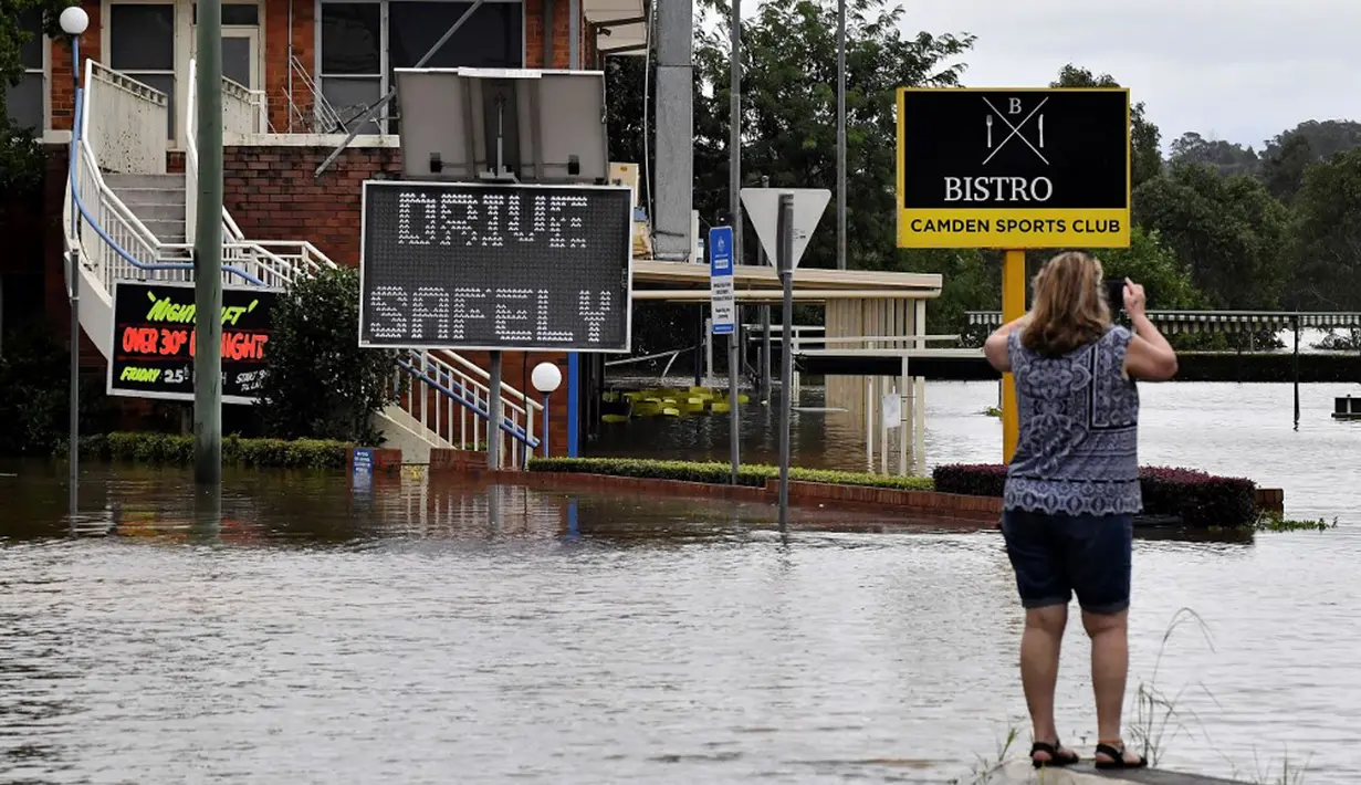 Seorang warga mengambil gambar meningkatnya air banjir akibat hujan deras di pinggiran barat daya Camden, Sydney, Australia, Selasa (8/3/2022). (Muhammad FAROOQ/AFP)