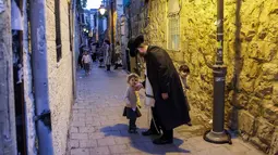 Seorang pria Yahudi Ultra-Ortodoks menyapa anak-anak saat berjalan di lingkungan Yerusalem (26/10/2020). (AFP/Emmanuel Dunand)