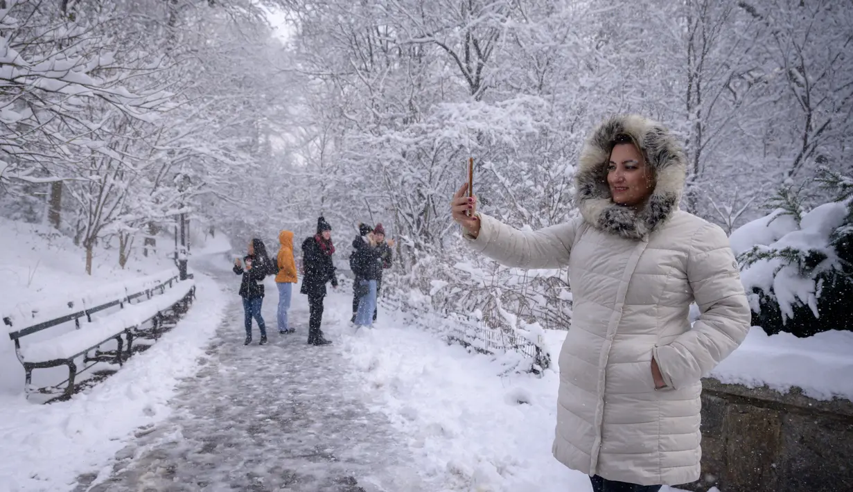 Orang-orang berpose di bawah pohon yang tertutup salju di Central Park setelah badai salju pertama musim dingin 2022 di New York City, Jumat (7/1/2022). Badai musim dingin membawa lebih dari 15 cm salju di bagian timur Amerika Serikat (AS), menutup sekolah, kantor dan jalan-jalan. (Ed JONES / AFP)