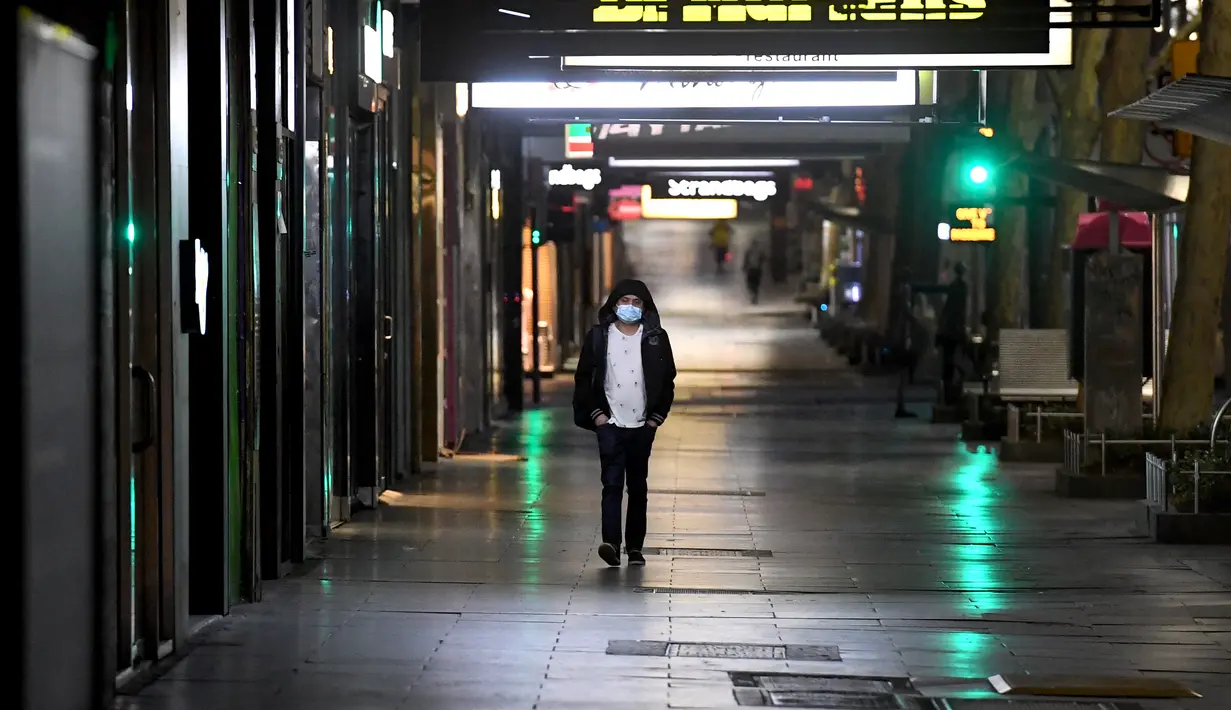Seorang pria berjalan di jalan yang sepi selama aturan jam malam di Melbourne, pada Selasa (17/8/2021). Kota terbesar kedua di Australia itu memberlakukan pembatasan tinggal di rumah pada pukul 9 malam hingga 5 pagi untuK meredam lonjakan Covid-19 varian Delta. (William WEST/AFP)