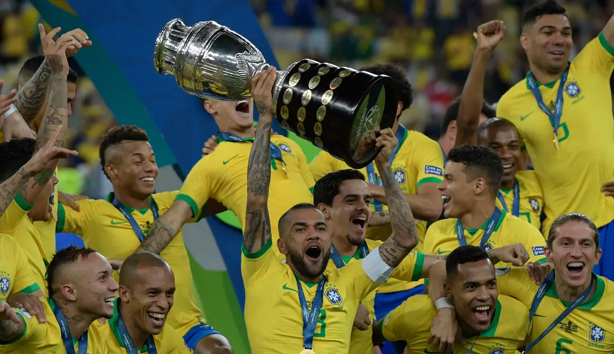 Pemain belakang timnas Brasil, Dani Alves mengangkat trofi Copa America 2019 saat berselebrasi bersama rekan setimnya setelah mengalahkan Peru pada partai final di Maracana Stadium, Rio de Janeiro, Senin (8/7/2019) dini hari WIB. Brasil menundukkan Peru dengan skor 3-1. (Juan MABROMATA/AFP)