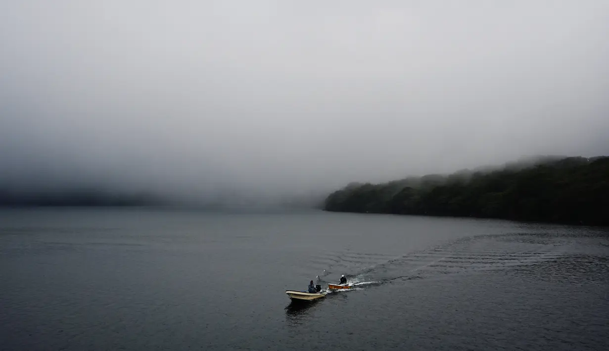 Dua pria mengendarai perahu di atas Danau Ashi di perfektur Kanagawa, Jepang (11/9/2019). Danau Ashi adalah sebuah sebuah danau cantik yang terletak pada wilayah Taman Nasional Hakone di Prefektur Kanagawa, Jepang. (AFP Photo/Charly Triballeau)