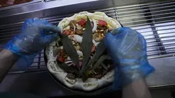 Daun ganja ditaruh di atas pizza di sebuah restoran di Bangkok, Thailand pada 24 November 2021. Produk ini menggunakan daun ganja dan legal untuk dikonsumsi, di mana seloyang pizza ganja berukuran 22 cm dihargai 499 baht atau Rp213 ribu. (AP Photo/Sakchai Lalit)