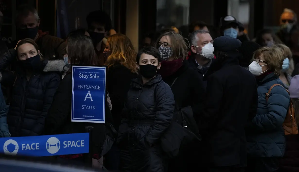 Orang-orang mengantre mengenakan masker melawan virus corona, di luar teater untuk pertunjukan Les Miserables di London, Selasa (28/12/2021). Di Inggris, pemerintah telah mengatakan bahwa tidak akan ada pembatasan baru sebelum Tahun Baru. (AP Photo/Alastair Grant)