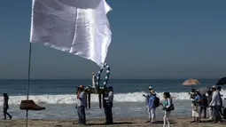 Warga setempat melakukan prosesi keagamaan dekat seni instalasi kontemporer "Tu huella es el camino, tu bandera es de paz" di Playas de Tijuana, Meksiko (7/10). (AFP Photo/Guillermo Arias)