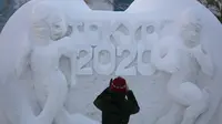 Seorang wanita memotret patung salju yang mempromosikan Tokyo 2020 selama Festival Salju Sapporo ke-71 di Taman Odori di Sapporo, Jepang, Selasa, (4/2/2020). Taman ini akan berfungsi sebagai titik awal dan akhir dari kedua perlombaan lari maraton dan di Olimpiade Tokyo 2020. (AP Photo/Jae C. Hong)