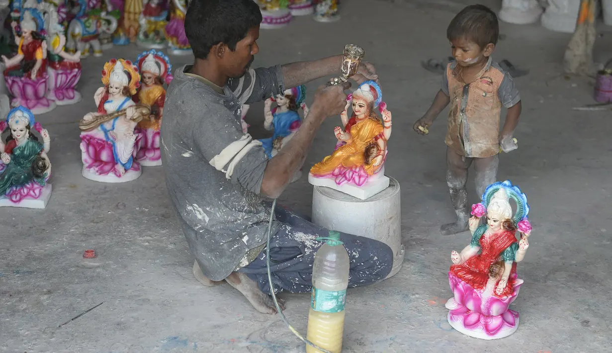 Seorang perajin bersama anaknya melukis patung dewi Hindu Lakshmi di sebuah bengkel menjelang Diwali, festival lampu Hindu di pinggiran Hyderabad (28/10/2021). Diwali merupakan festival cahaya yang dianggap banyak orang sebagai awal tahun baru. (AFP/Noah Seelam)