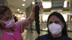 Maryori Araque (kanan) melihat sehelai rambutnya setelah dipotong dalam acara Bulan Peduli Kanker Payudara di sebuah mal di Caracas, Venezuela, Sabtu (16/10/2021). Rambut yang dipotong akan disumbangkan untuk membuat wig bagi pasien kanker. (AP Photo/Ariana Cubillos)