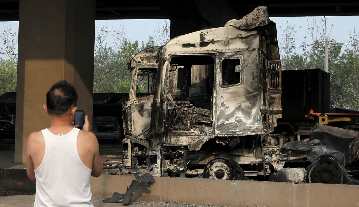 Warga mengambil gambar kendaraan yang rusak di dekat lokasi ledakan di pelabuhan Kota Tianjin, China, Kamis (13/8/2015). Ledakan yang diperkirakan berkekuatan setara 21 ton TNT ini menewaskan 17 orang dan ratusan lainya terluka. (REUTERS/Stringer)