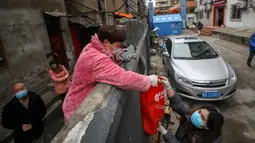 Seorang penduduk menerima sekantong makanan di atas tembok di Wuhan di provinsi Hubei tengah China (3/3/2020). Wuhan merupakan kota di China yang menjadi awal mula wabah virus corona. (AFP/STR)