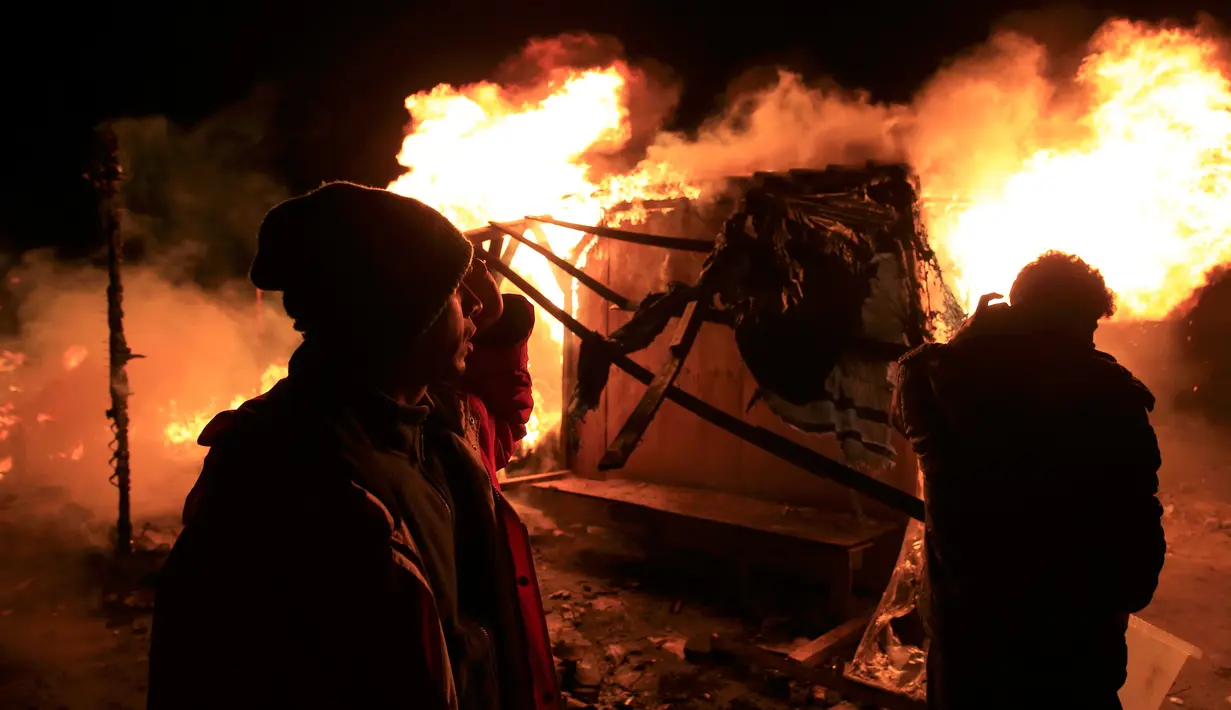 Sejumlah imigran berdiri melihat tempat tinggalnya yang dibakar pihak berwenang Prancis saat pembongkaran kamp pengungsian di lahan kumuh yang dijuluki "Jungle" di Calais, Prancis (1/3). (REUTERS/Pascal Rossignol)