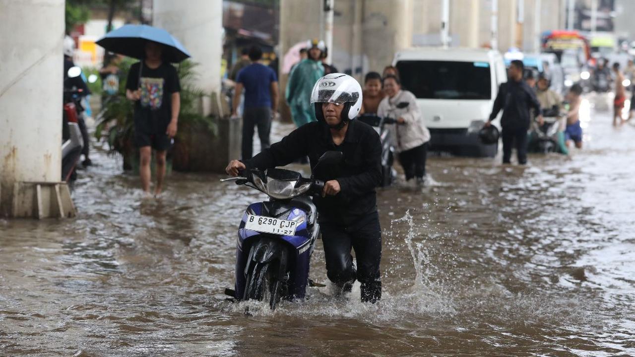 Seorang warga mendorong sepeda motornya yang mogok saat melewati banjir di Jalan Ciledug Raya, Jakarta Selatan, Sabtu (6/7/2024). Hujan deras yang mengguyur wilayah Jakarta sejak pagi hari tadi menyebabkan Jalan Ciledug Raya kembali terendam banjir.&nbsp;