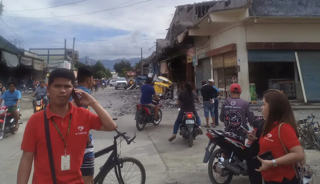 Penduduk berdiri di samping bangunan yang rusak setelah gempa melanda Padada, provinsi Davao del Sur, Filipina (15/12/2019). Gempa menyebabkan bangunan tiga lantai runtuh dan membuat warga panik bergegas keluar dari pusat perbelanjaan, rumah dan bangunan lain. (AP Photo/John Angelo Jomao-as)