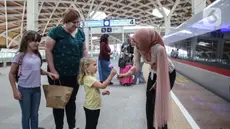 Petugas perempuan Kereta Cepat Whoosh mengenakan kebaya sambil membagikan bunga kepada calon penumpang di Stasiun Halim Whoosh, Jakarta, Senin (21/4/2025). (Liputan6.com/Angga Yuniar)