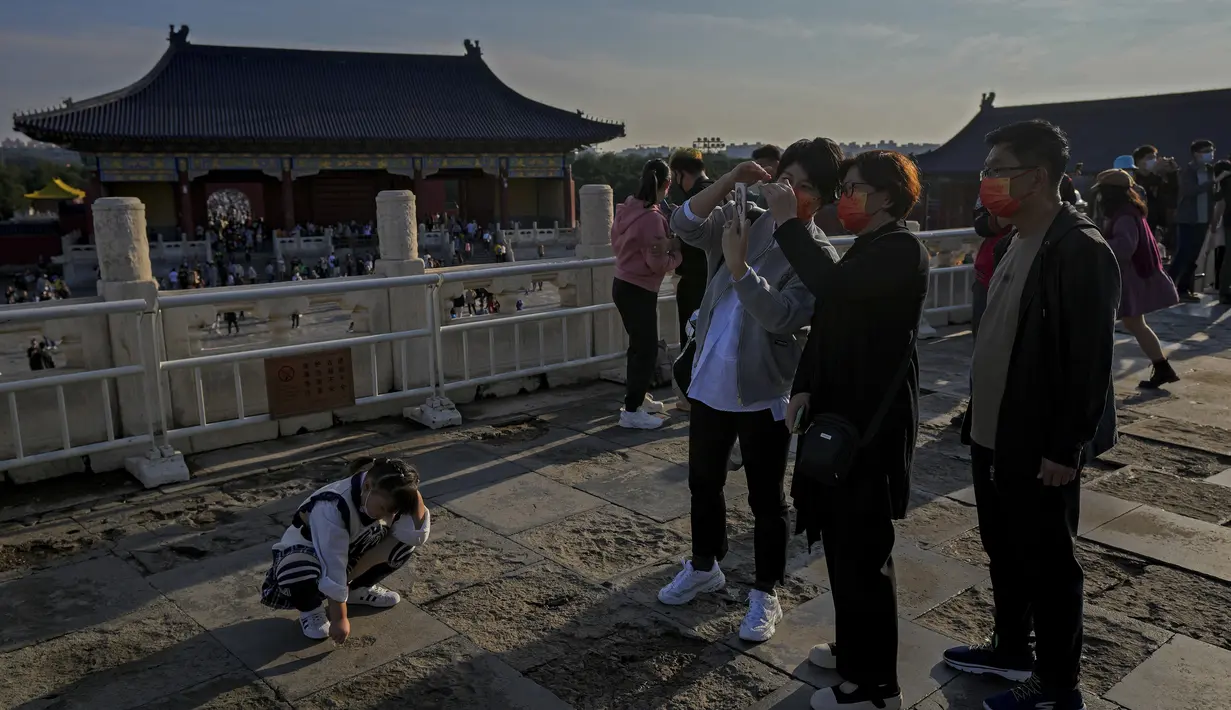 Seorang anak bereaksi ketika kerabatnya melihat-lihat foto smartphone mereka saat pengunjung mengunjungi Kuil Surga pada hari terakhir Hari Nasional China selama seminggu di Beijing, Kamis (7/10/2021). (AP Photo/Andy Wong)
