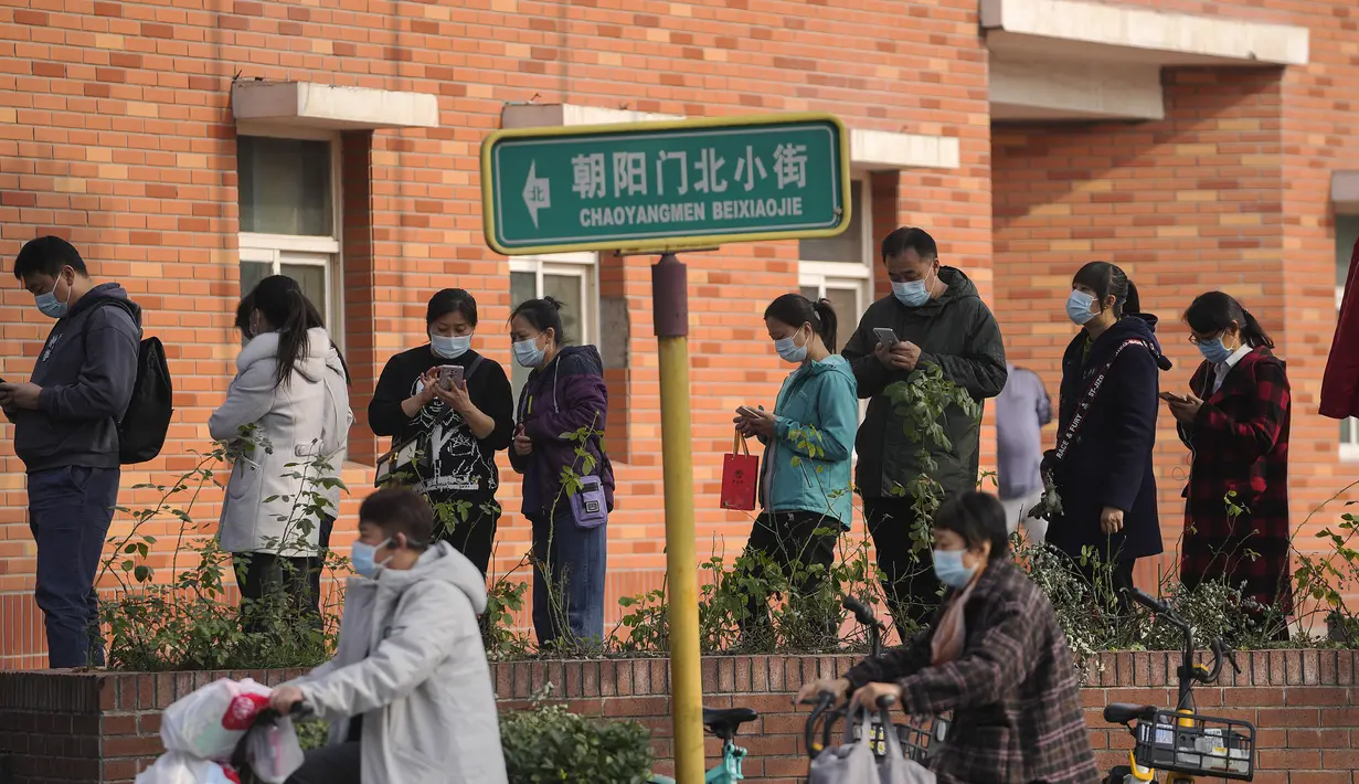Pengendara skuter melewati warga yang antre untuk menerima suntikan booster di tempat vaksinasi di Beijing, Senin (25/10/2021). Sebuah provinsi di China barat laut yang sangat bergantung pada pariwisata menutup semua lokasi wisata pada Senin setelah menemukan kasus baru COVID-19 (AP Photo/Andy Wong)