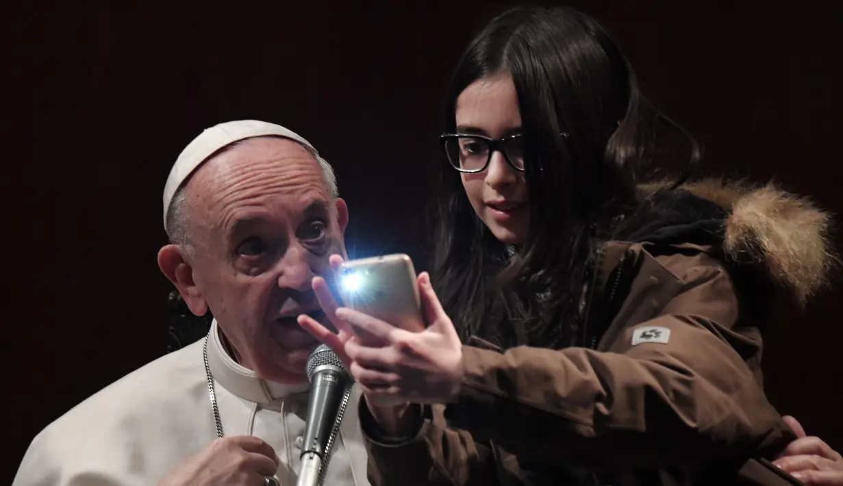 Seorang anak perempuan tidak mau ketinggalan berfoto selfie dengan Paus Fransiskus dalam kunjungannya ke St Mary Josefa di Roma, Italia, Minggu (19/2). (AFP Photo/TIZIANA FABI)