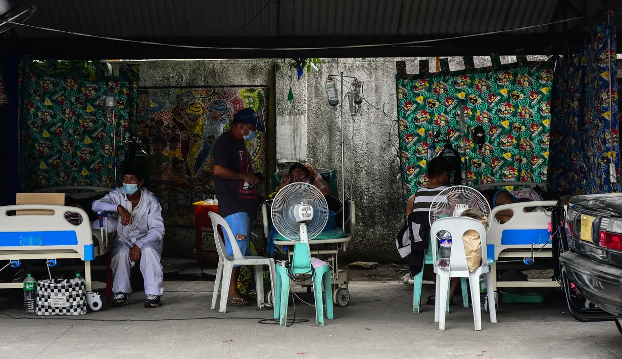 Kerabat pasien terduga Covid-19 duduk di samping tempat tidur mereka sambil menunggu di tempat parkir yang diubah menjadi bangsal di luar rumah sakit di kota Binan, Manila, di tengah rekor infeksi yang dipicu oleh varian Delta yang sangat menular pada Senin (6/9/2021). (Photo by Maria Tan / AFP)