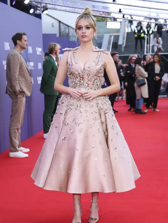Aimee Lou Wood berpose di depan fotografer saat tiba untuk pemutaran perdana film 'Living' selama Festival Film London 2022 di London, Minggu, 9 Oktober 2022. Bintang Sex Education berusia 27 tahun itu tampil glamor dalam balutan gaun rose gold dengan detail permata. (Photo by Vianney Le Caer/Invision/AP)