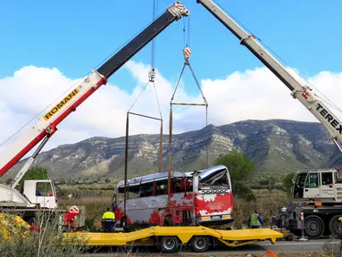 Dua crane dikerahkan untuk mengevakuasi sebuah bus di Jalan Raya AP7 dekat Kota Freginals, Spanyol, Minggu (20/3). Bus berisi 57 penumpang yang mayoritas mahasiswa asing itu terbalik ketika dalam perjalanan dari Valencia menuju Barcelona (PAU Barrena/AFP)