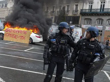 Plakat bertuliskan "Polisi antihuru-hara, pergi" ditempatkan pada mobil yang terbakar saat polisi antihuru-hara mengamankan demonstrasi di Rennes, Prancis, Kamis (13/4/2023). (AP Photo/Mathieu Pattier)