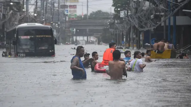 Orang-orang menyeberangi banjir melewati bus penumpang yang setengah terendam di sebuah jalan di Manila, Filipina. [Ted Aljibe/AFP]