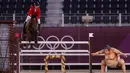 Atlet berkuda Kanada Mario Deslauriers mengendarai Bardolina 2 melewati patung pesumo dalam kualifikasi individu lompat berkuda Olimpiade Tokyo 2020 di Equestrian Park di Tokyo (3/8/2021). Pihak panitia memasang patung simbol Jepang seperti sakura sampai pesumo di arena lintasan. (AFP/Behrouz Mehri)