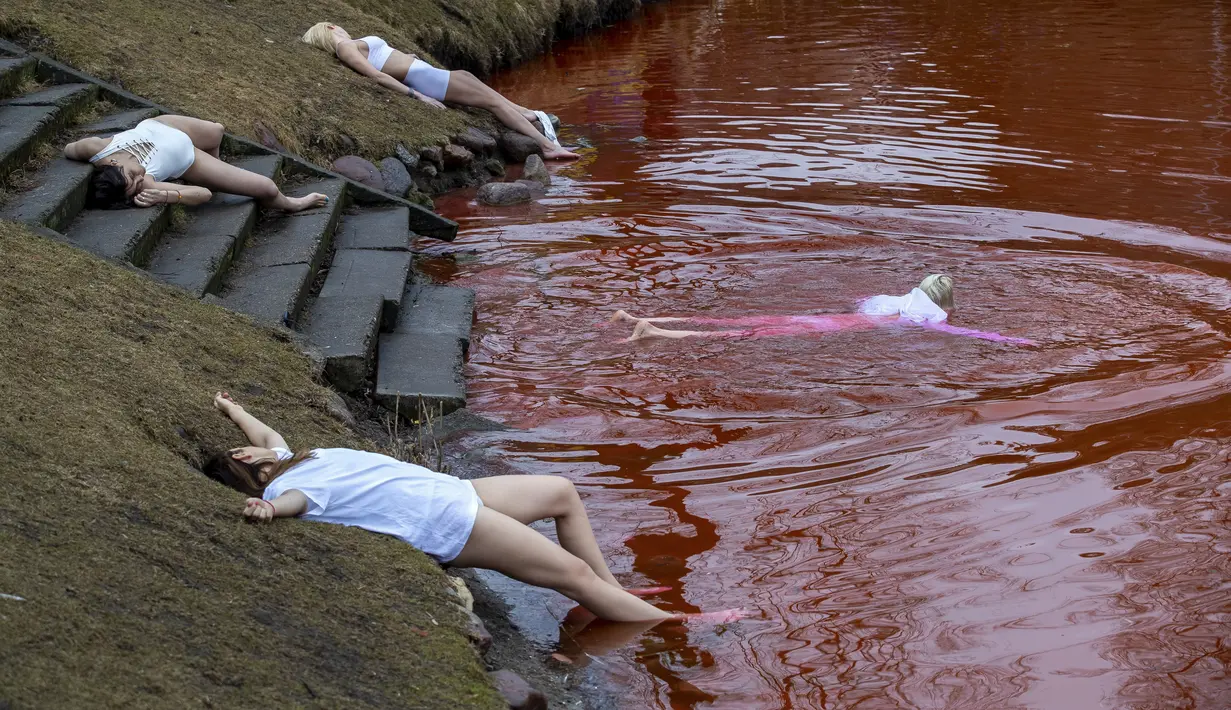 Orang-orang berbaring di tanah untuk melambangkan mereka yang tewas dalam perang di Ukraina selama protes terhadap invasi Rusia, di dekat kolam berwarna merah untuk menandakan darah di depan kedutaan besar Rusia di Vilnius, Lithuania, Kamis (7/4/2022). (AP Photo/Mindaugas Kulbis)