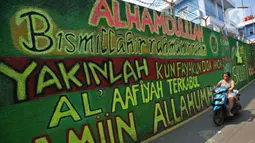 Pengendara melintasi mural bernuansa Islami di Gang Pelangi, kawasan Kalibata, Jakarta, Jumat (23/4/2021). Mural bernuansa Islami tersebut dibuat untuk menghiasi dan meramaikan pintu masuk gang sekaligus mengingatkan masyarakat untuk selalu beribadah dan bershalawat (Liputan6.com/Herman Zakharia)