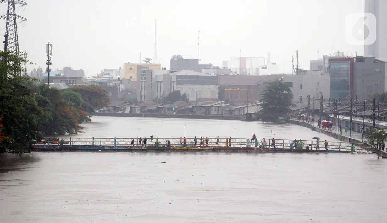 Warga berdiri di salah satu jembatan penghubung Banjir Kanal Barat di Kawasan Tanah Abang, Jakarta, Rabu (1/1/2020). Hujan yang mengguyur Jakarta sejak Selasa sore (31/12/2019) mengakibatkan debit air Banjir Kanal Barat tinggi dan hampir meluap. (Liputan6.com/Helmi Fithriansyah)